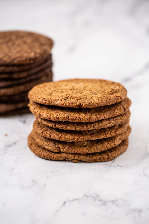 A close-up of a stack of golden-brown round Chocolate Chunk Cookies on a white marble surface, with a second stack blurred in the background.