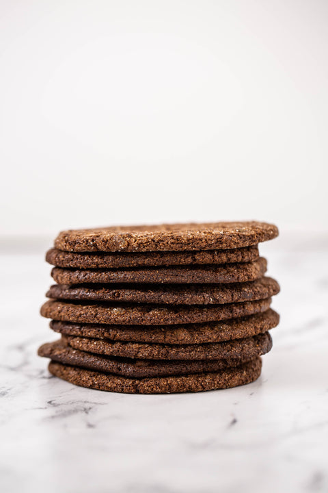 A stack of round, textured brown Several round Ginger Molasses Cookies scattered on a white marble surface, photographed from above.cookies on a white marble surface with a clean white background.