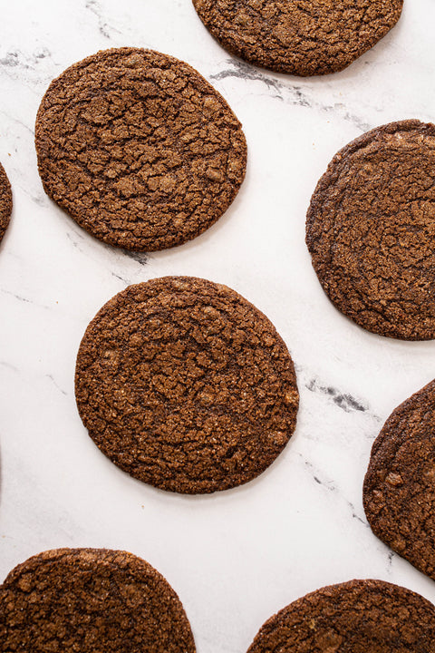Several round Ginger Molasses Cookies Bag of 5 scattered on a white marble surface, photographed from above.
