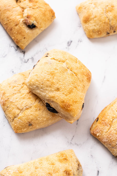 Golden-brown baked scones with dark olive pieces, arranged on a white marble surface.