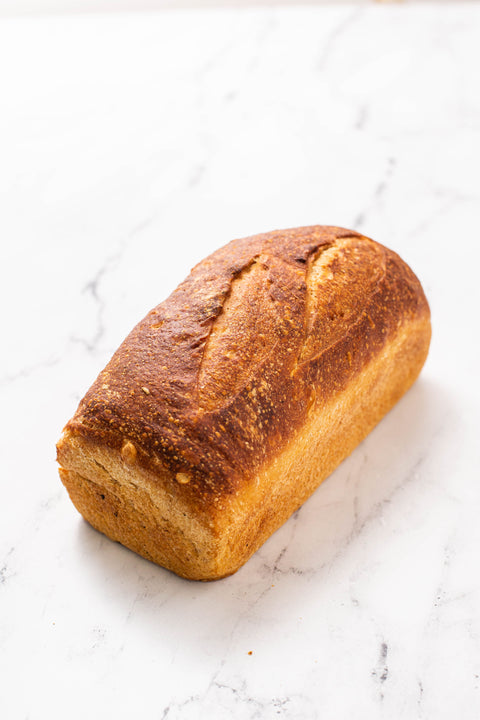 A single rustic peasant french loaf of bread with a golden-brown crust sits on a white marble surface.