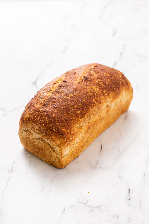 A single rustic loaf of bread with a golden-brown crust sits on a white marble surface.
