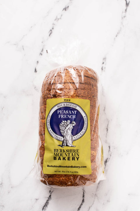 A loaf of Berkshire Mountain Bakery Peasant French bread in clear plastic packaging with a yellow label, placed on a white marble surface.